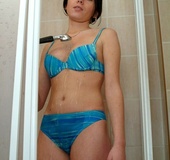 Busty black haired gal in blue bikini slowly undressing in the shower