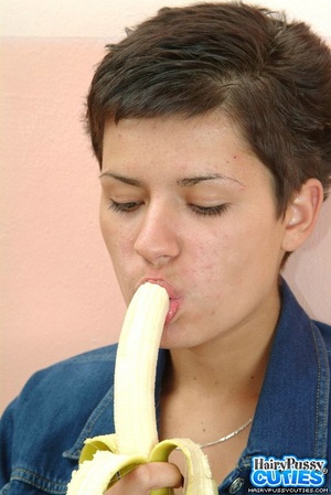 Short haired brunette in black undies and jeans outfit eating banana before posing naked on the table and fingering her bushy cunt - Picture 7