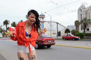 Foxy chick displays her smoking hot body while she eats her burger and fries as she walks around the street wearing her orange shirt, puple bra, white shorts and black high heels. - Picture 10
