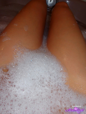 Wet brunette with blue eyes scrubbing her body in a bathtub - Picture 2