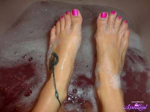 Wet brunette with blue eyes scrubbing her body in a bathtub - Picture 3