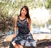 Innocent brunette sirs on a wooden bench and lifts her flowy skirt outside