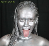 Weird slut covered in  silver paint lays on the black floor and shoves