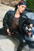 Tall biker girl in leather uniform and bandanna strips outdoors by the