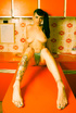 Amazing girl with tattoos poses naked on the kitchen countertop.