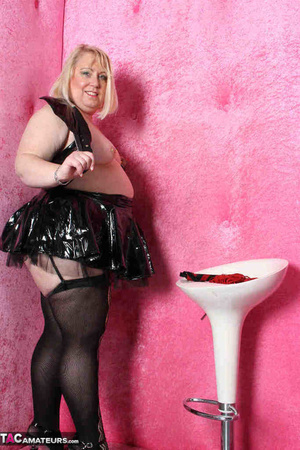 Big blonde in black leather outfit and black stockings stripteasing by the pink wall and showing her pierced vagina - XXXonXXX - Pic 10