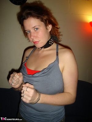 Collared redhead with blue eyes wearing gag ball and handcuffs before posing naked on the blue couch - Picture 1