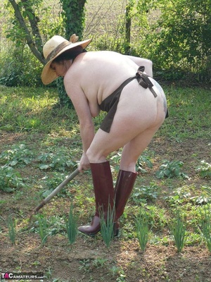 Dark haired wife with huge hooters working in the garden and showing her shaved pussy while posing in rubber boots - Picture 11
